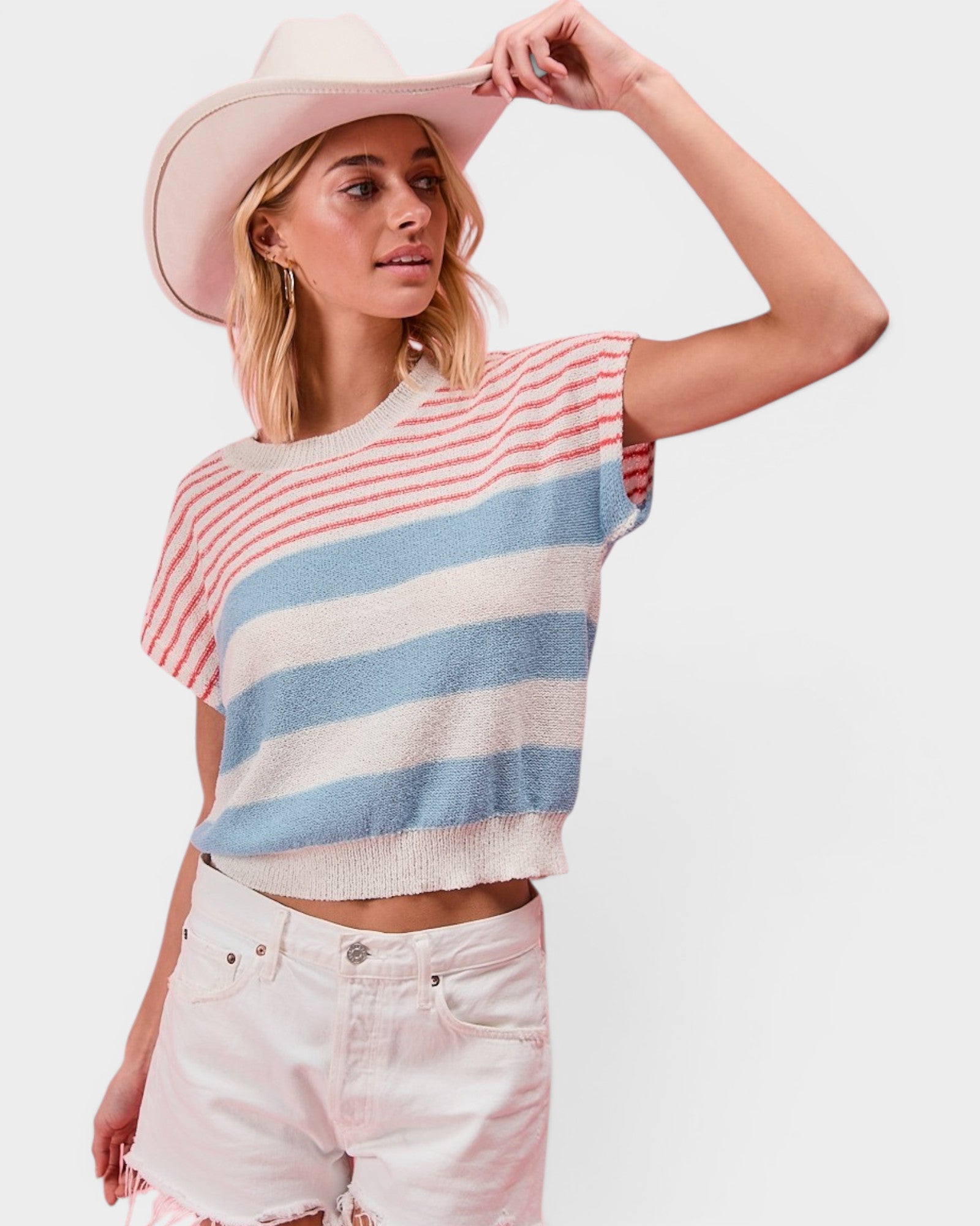 Woman wearing a striped sleeveless top and white shorts with a pink hat on a light background