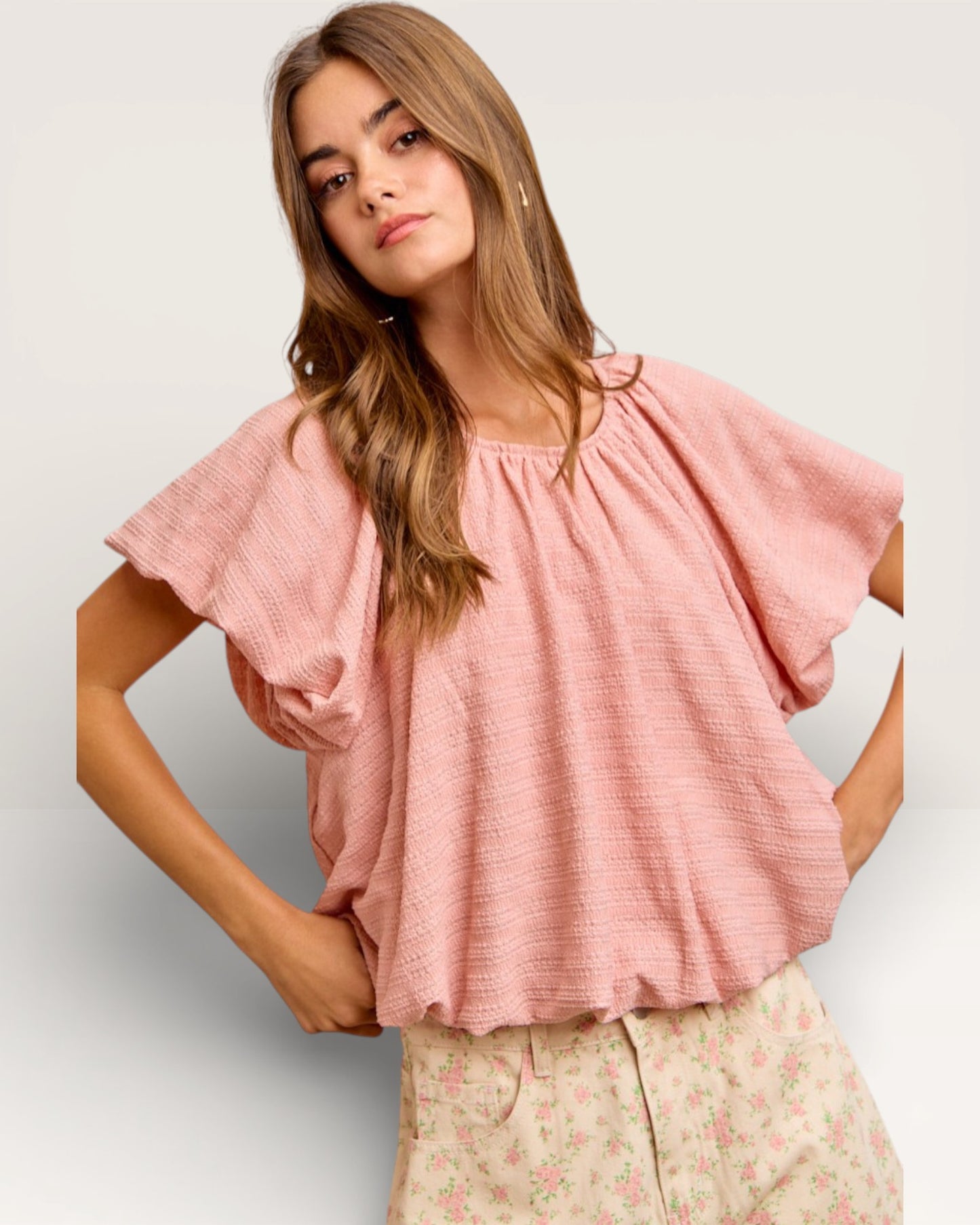 Woman wearing a pink blouse with ruffled sleeves on a plain background