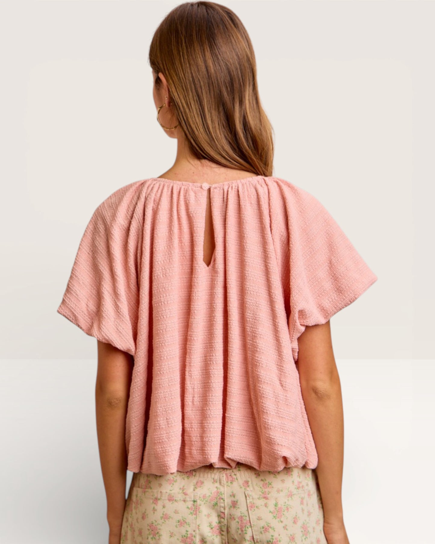 Woman wearing a pink blouse with a cutout back on a plain background
