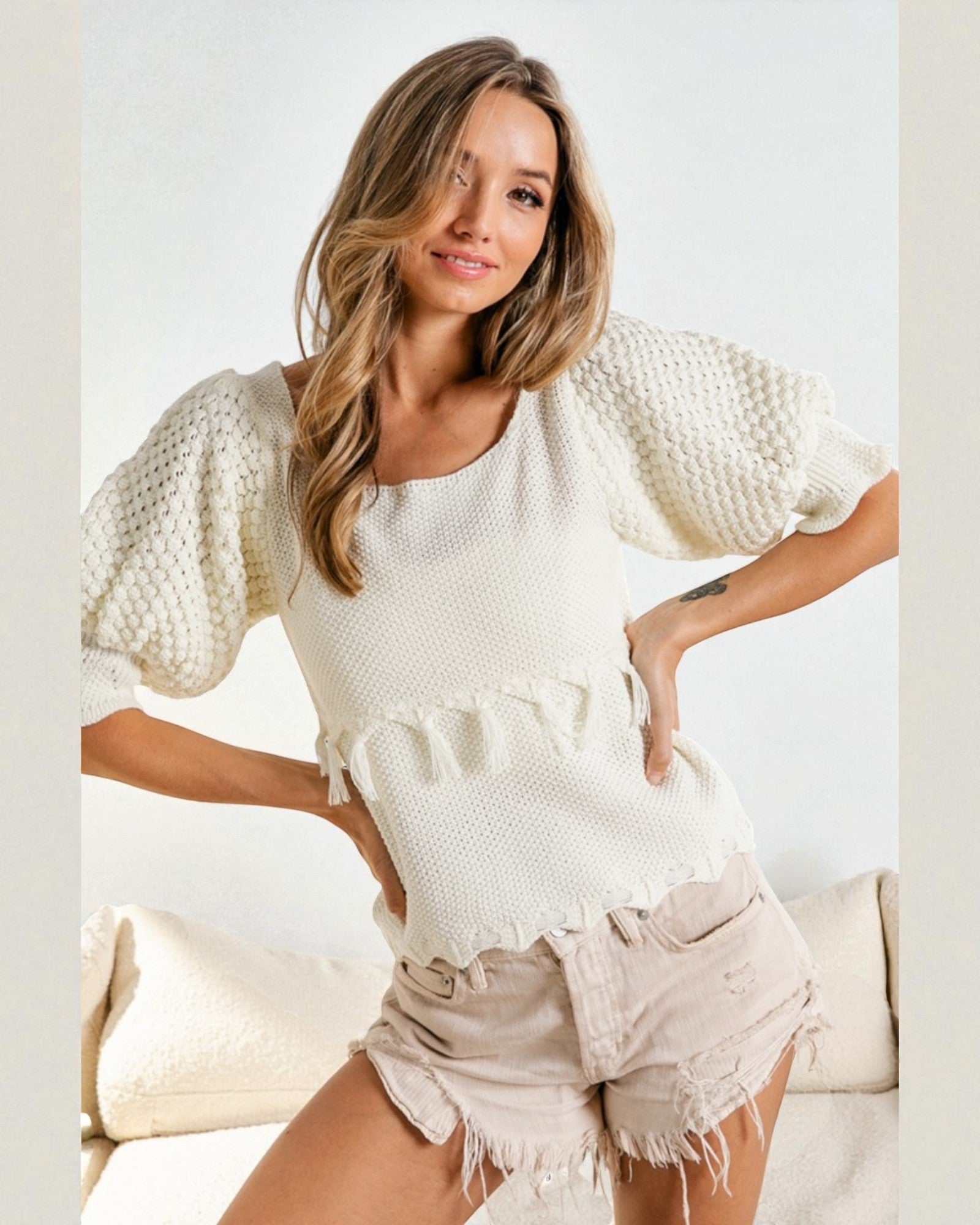 Woman wearing a white textured top and beige shorts on a light background