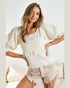 Woman wearing a white textured top and beige shorts on a light background
