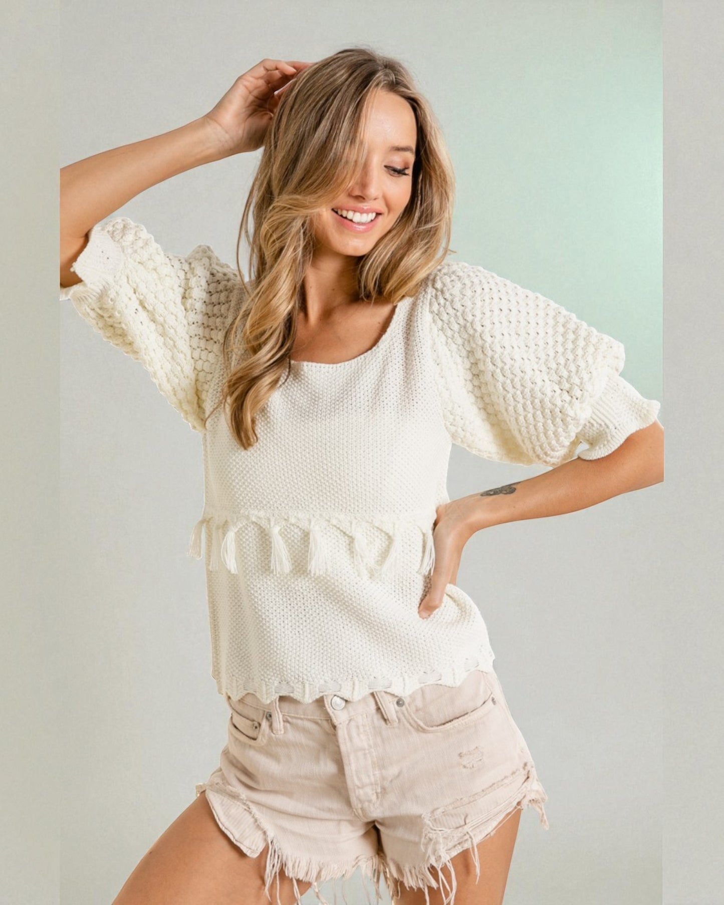 Woman wearing a white textured top and beige shorts against a light background