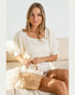 Woman sitting on a couch holding a woven bag with a white background