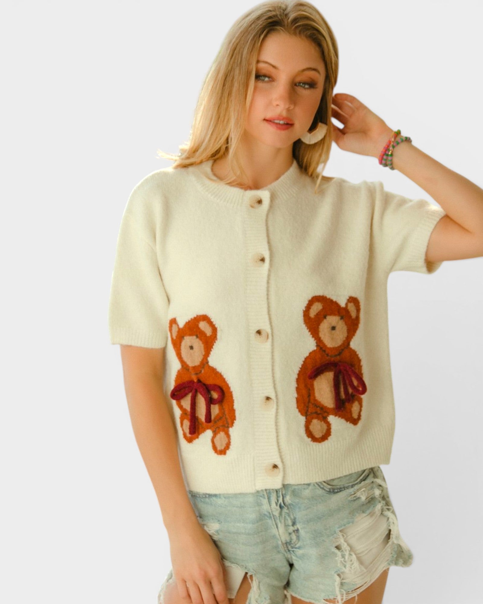 Woman wearing a cream cardigan with teddy bear designs on a white background