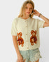 Woman wearing a cream cardigan with teddy bear designs on a white background