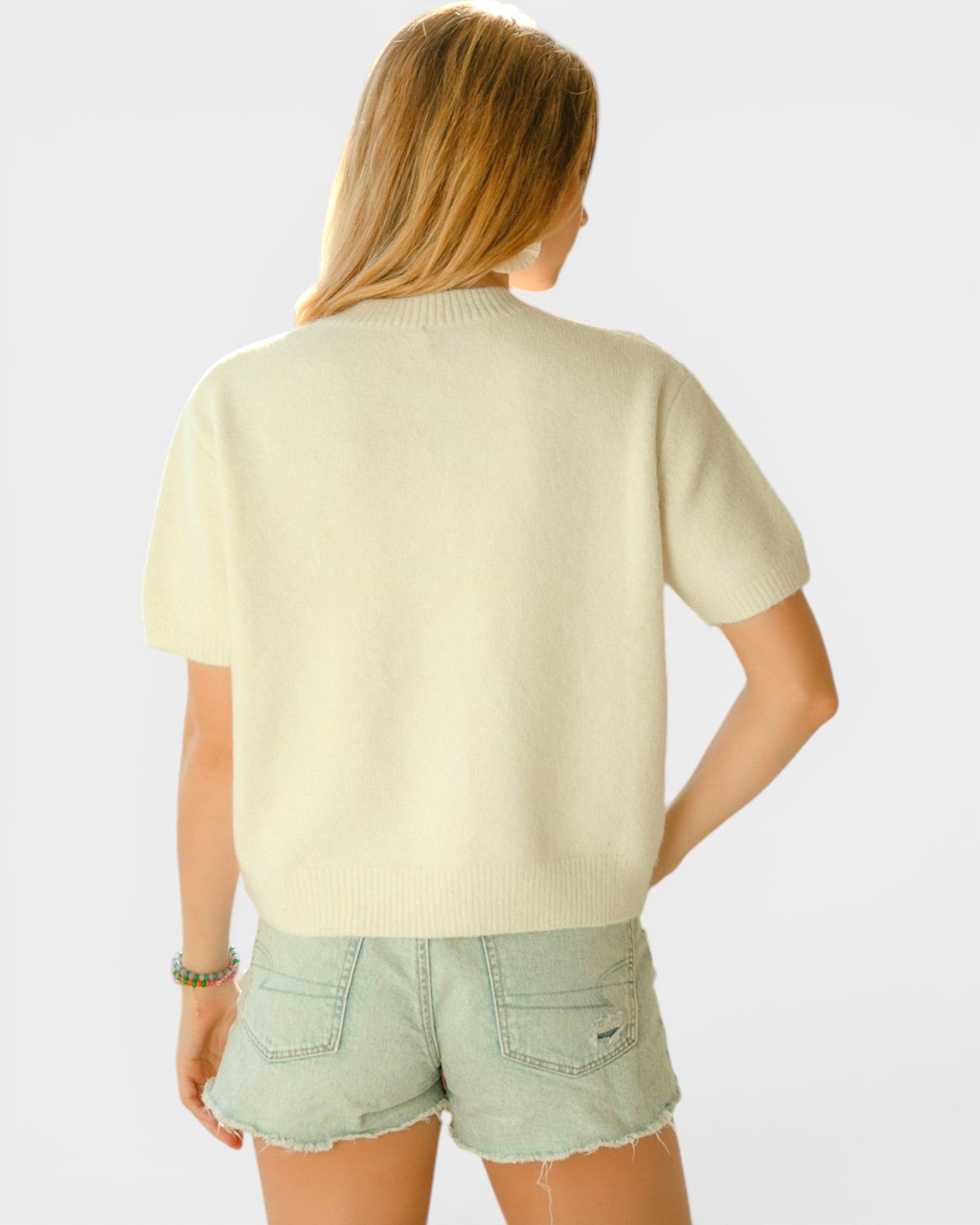 Person wearing a light green sweater and denim shorts on a white background