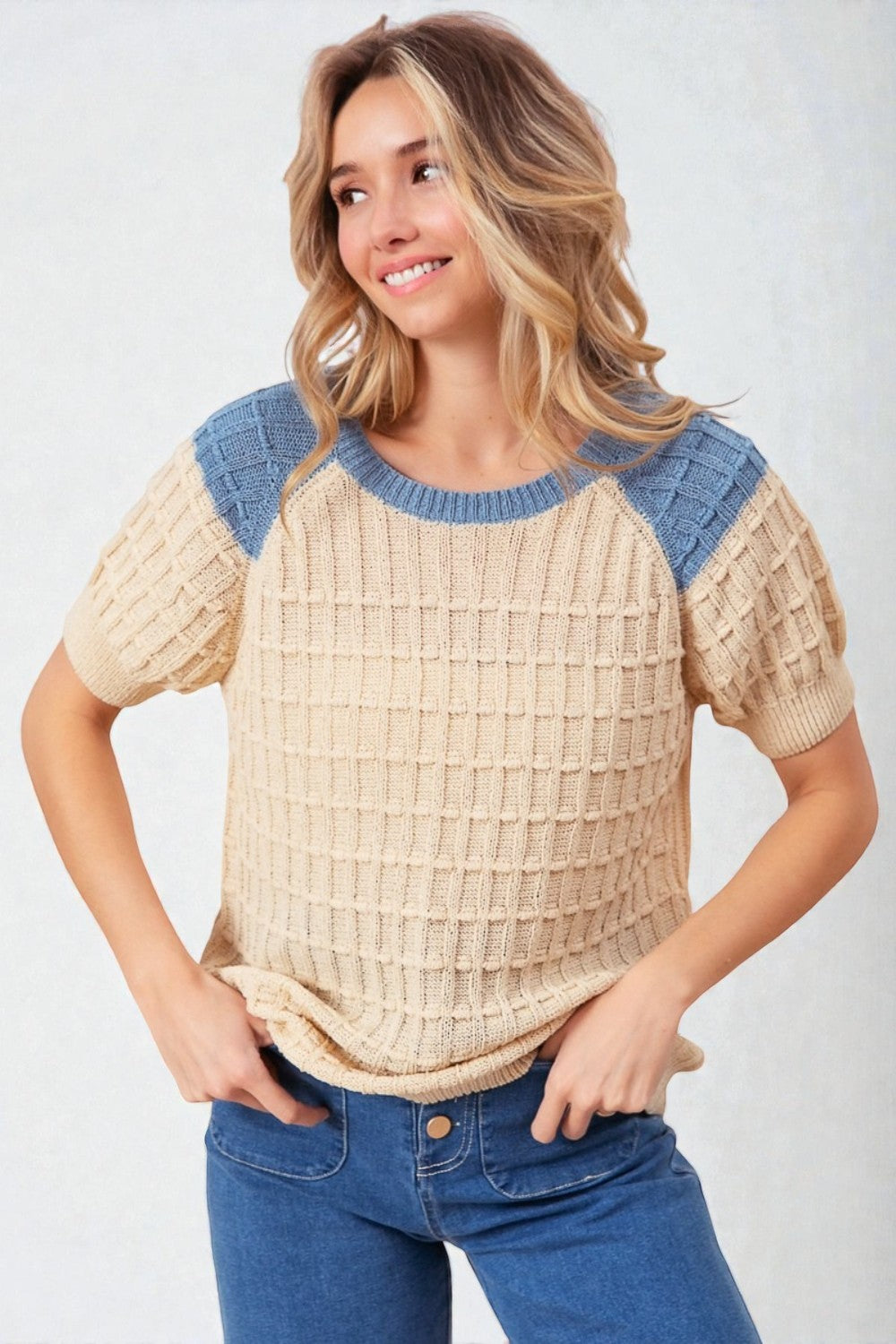 Woman wearing a beige and blue patterned top with blue jeans on a white background