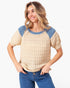 A woman wearing a beige and blue short-sleeve knit sweater with textured waffle patterns, paired with blue jeans, against a plain white background.