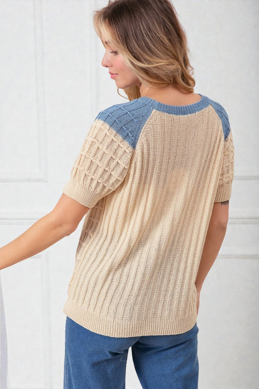 Woman wearing a beige sweater with blue accents against a white background