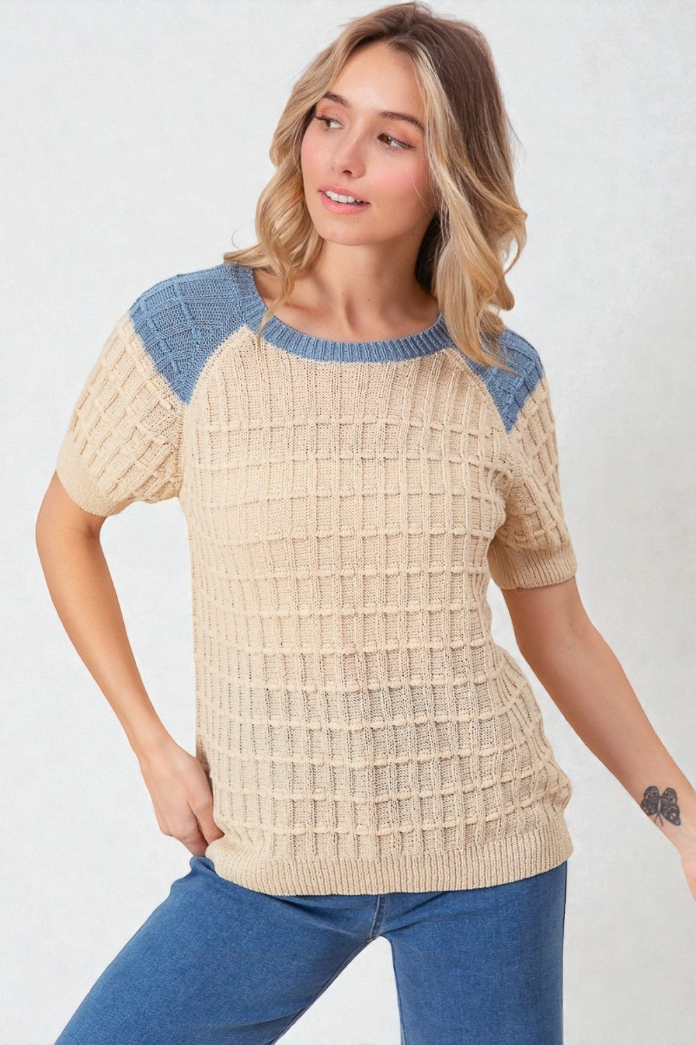 Woman wearing a beige sweater with blue accents on a white background