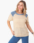A woman wearing a short-sleeve knit top with a beige waffle texture and blue raglan shoulder panels, paired with blue jeans, against a plain white background.