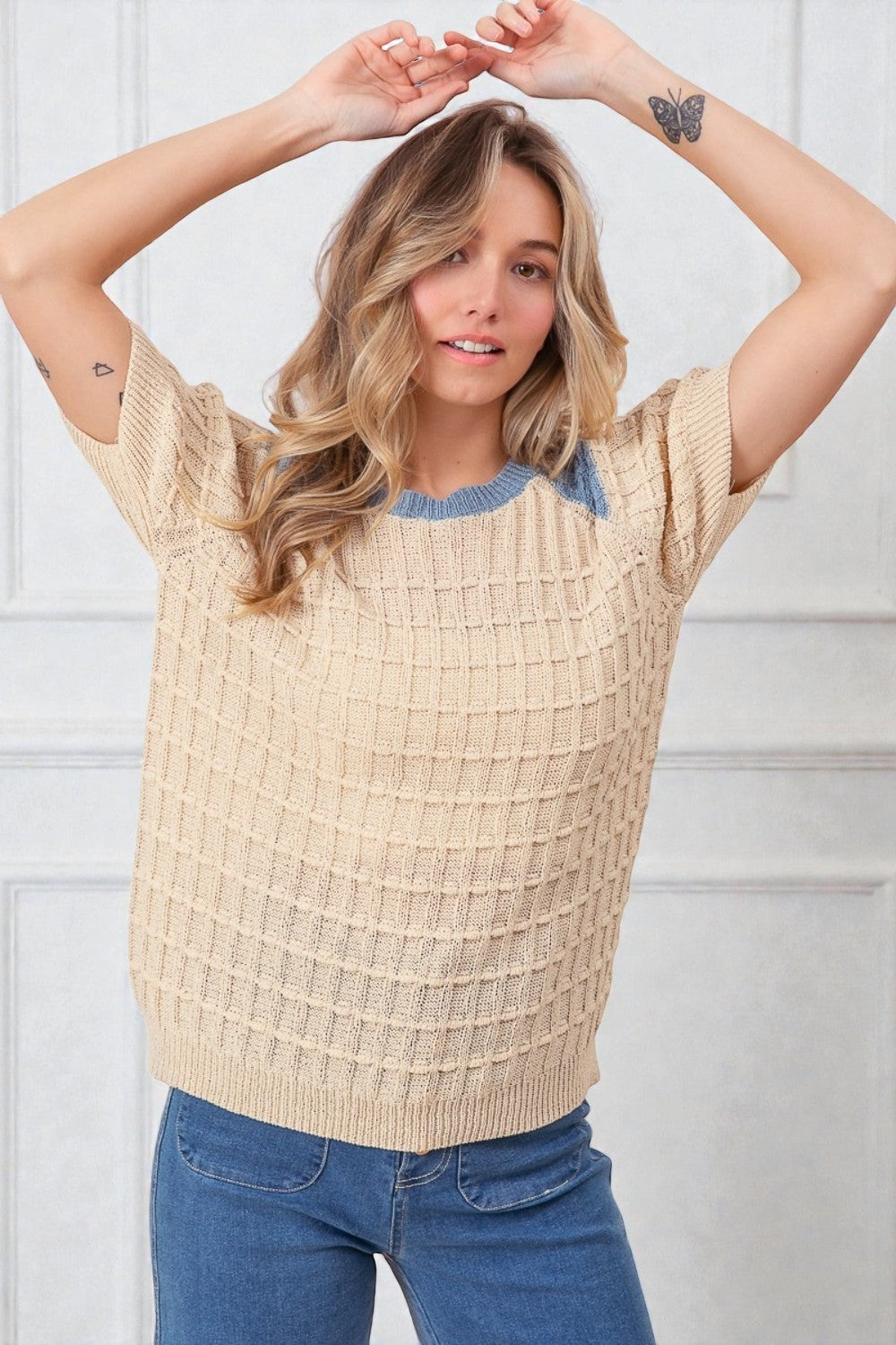 Woman wearing a beige textured sweater with blue trim against a white background