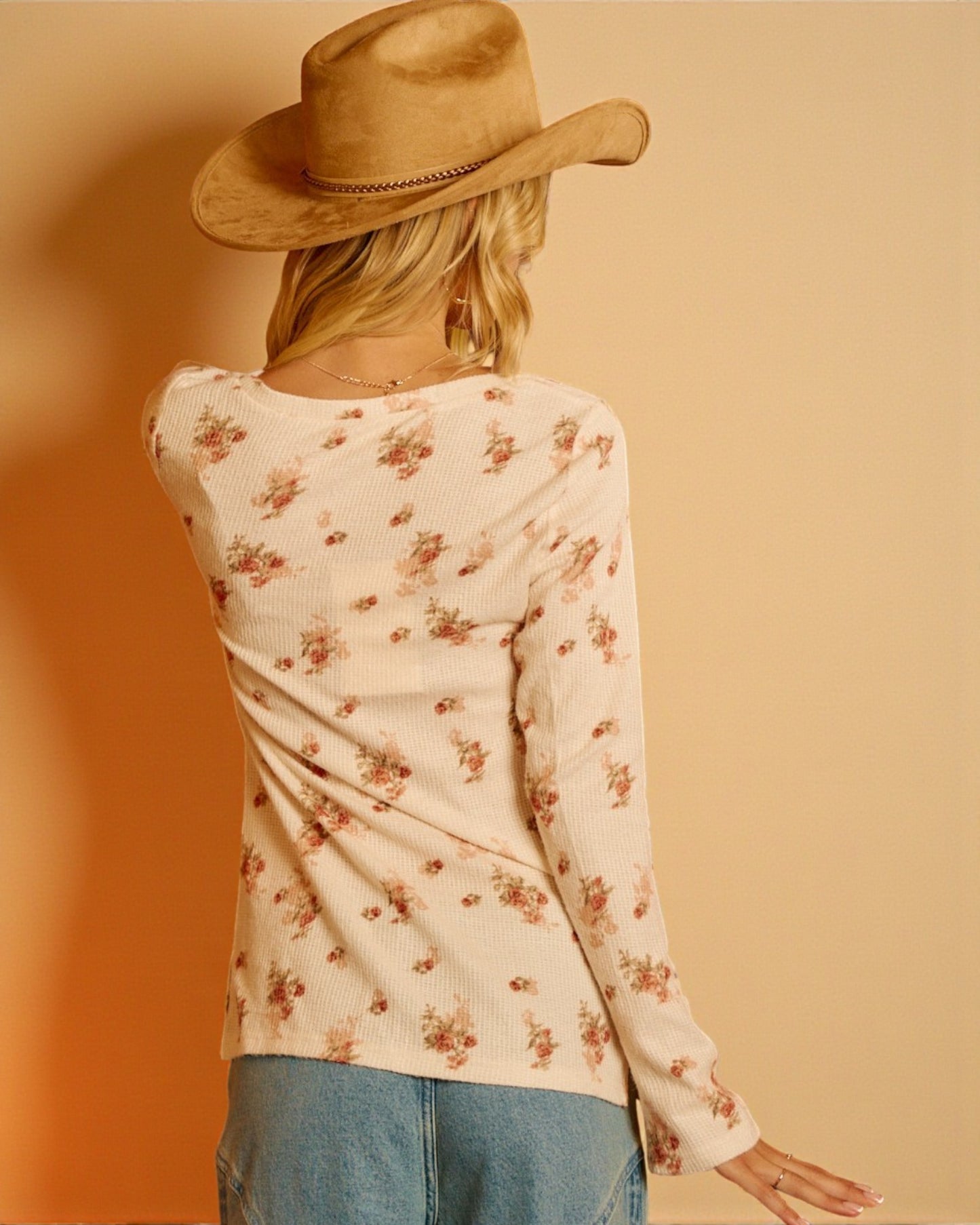 Person wearing a floral long-sleeve top and cowboy hat against a warm-toned background