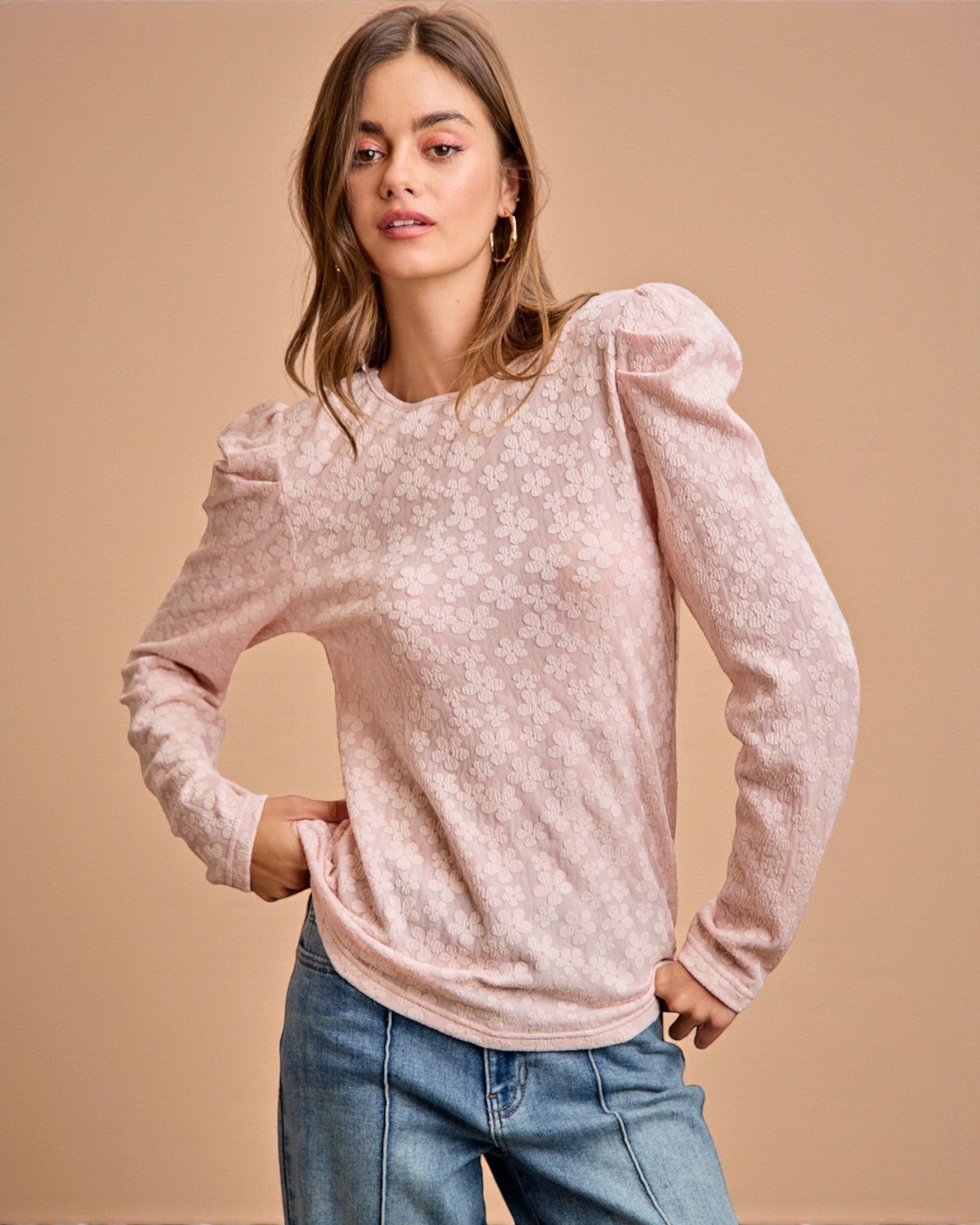 Woman wearing a pink long-sleeve top with puff sleeves against a beige background