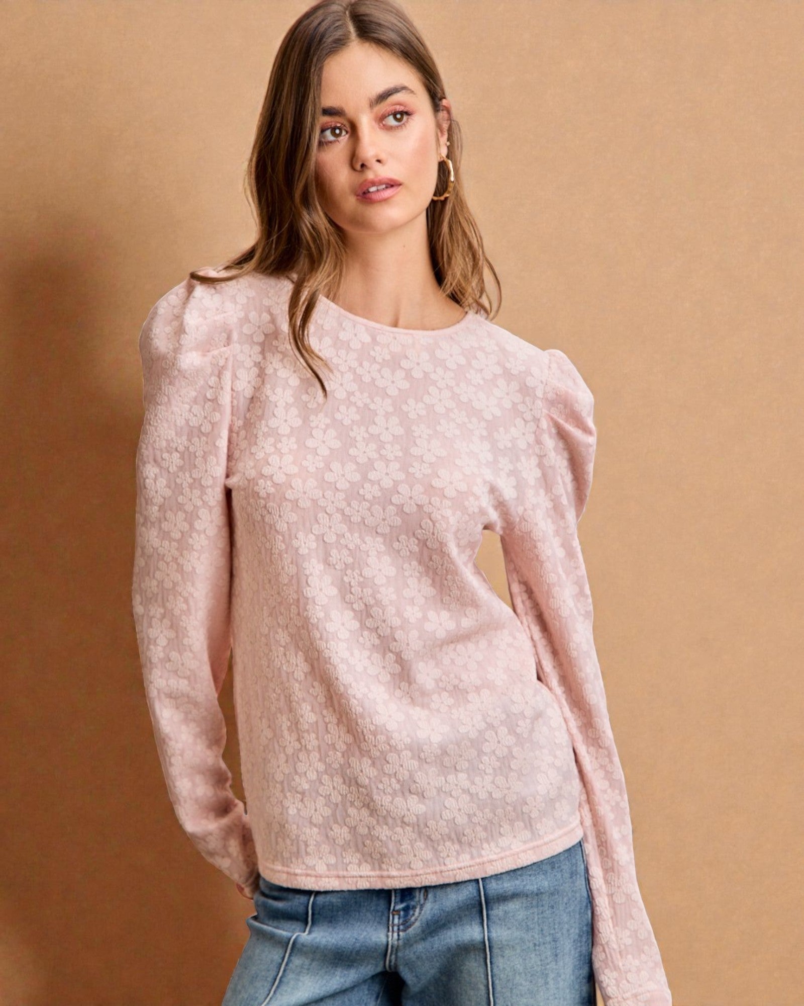 Woman wearing a light pink sweater with puffed sleeves against a beige background