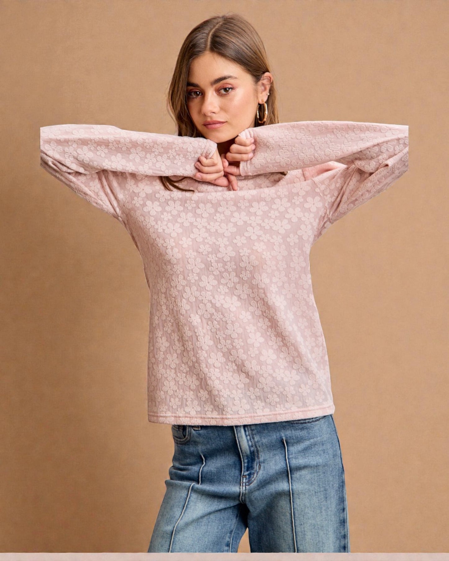 Woman wearing a light pink patterned sweater and blue jeans against a brown background