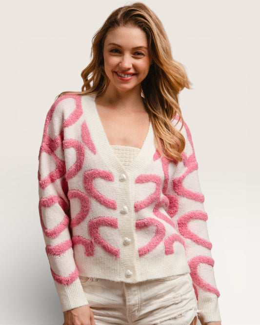 Woman wearing a white cardigan with pink heart patterns on a plain background