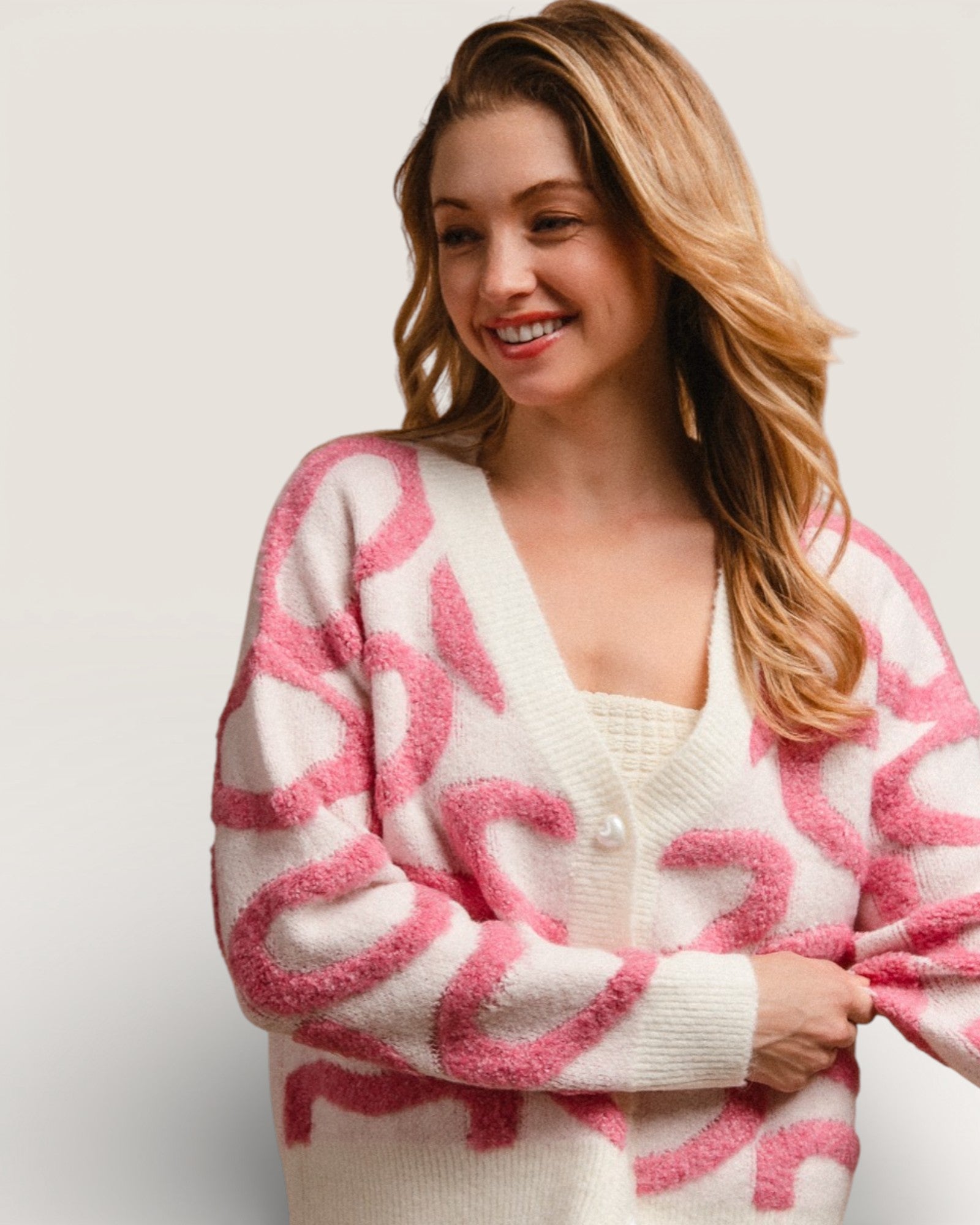 Woman wearing a white sweater with pink heart patterns on a plain background