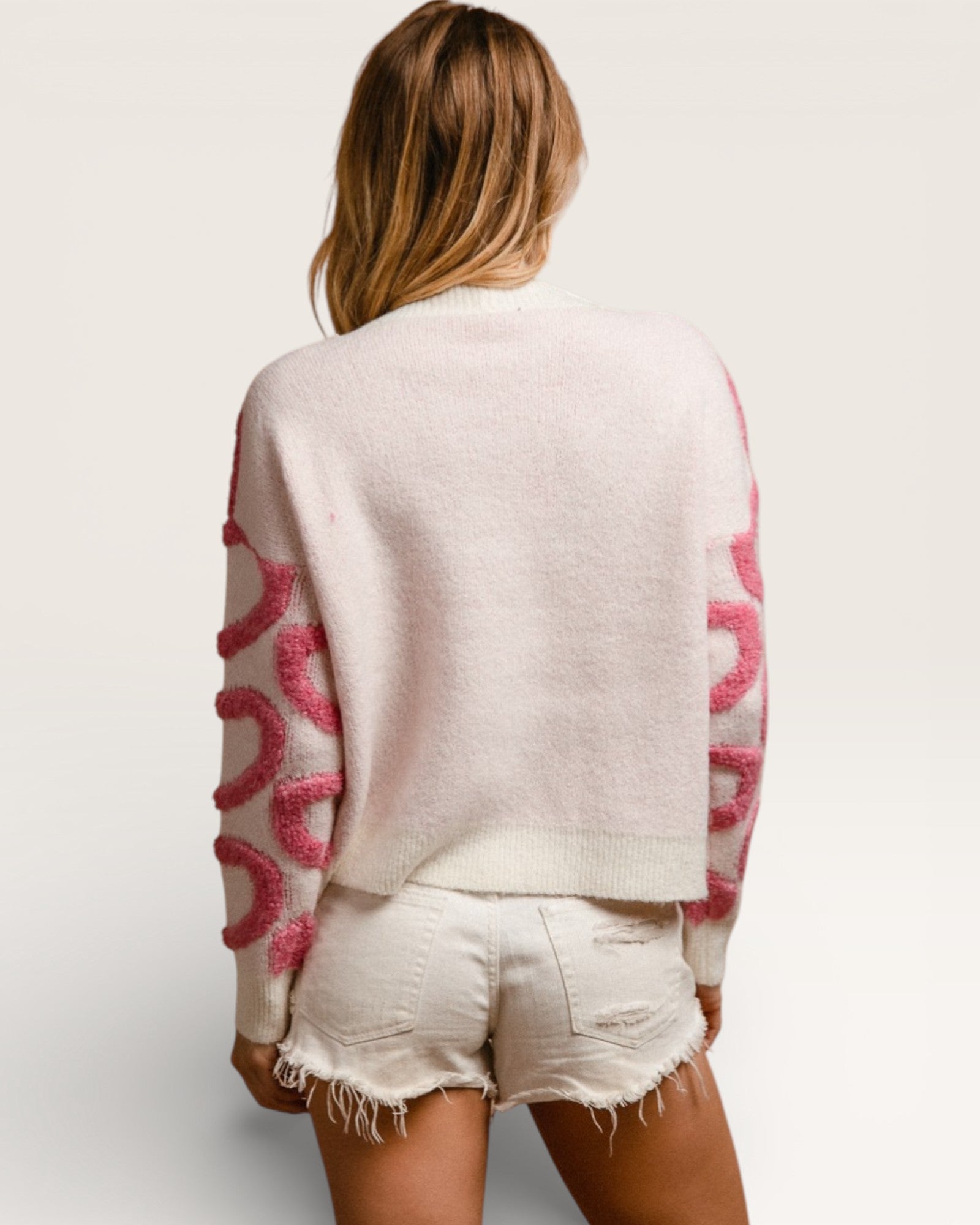 Person wearing a light-colored sweater with pink patterns and white shorts on a plain background