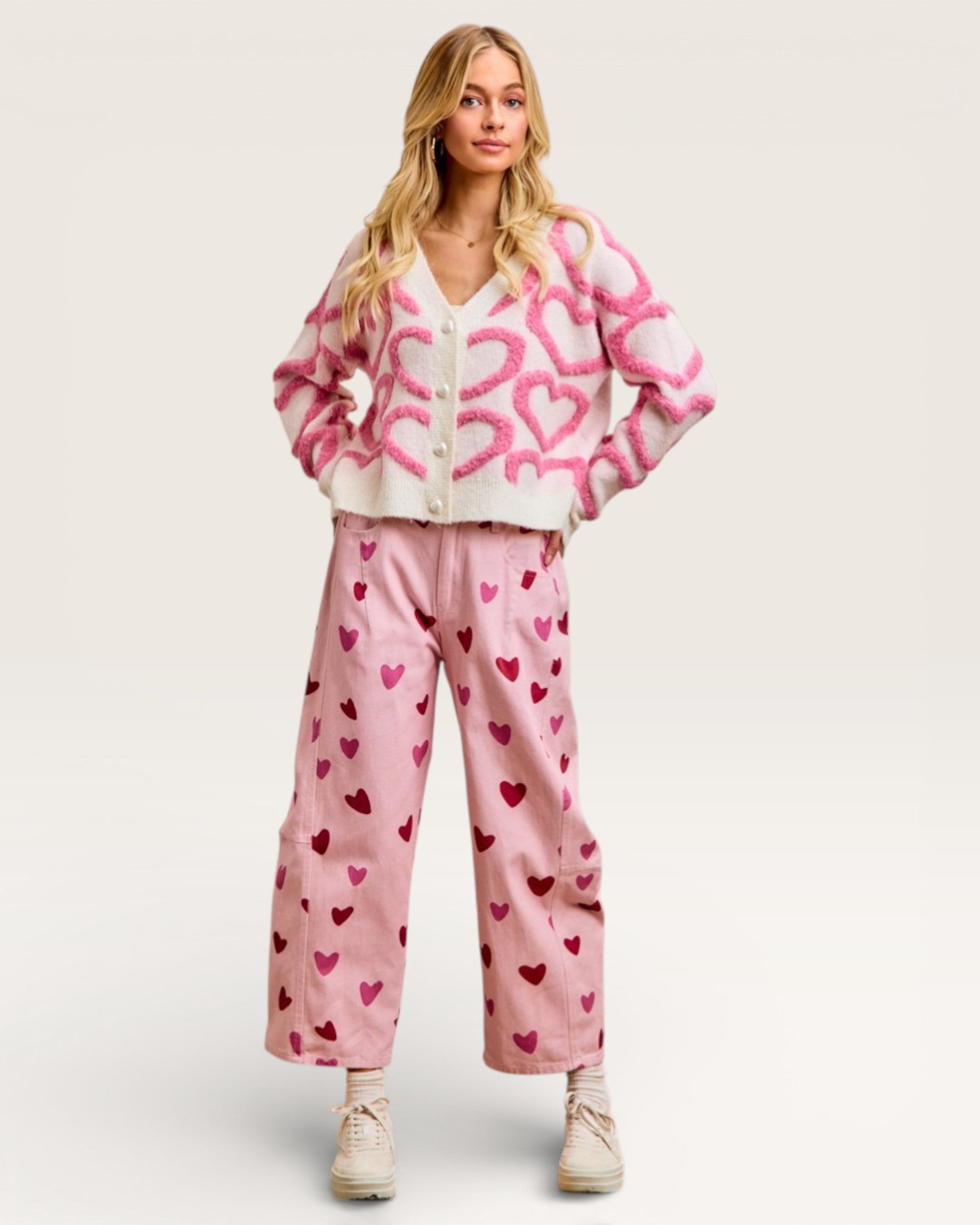 Woman wearing a pink and white cardigan with a pattern and pink pants with heart designs on a white background