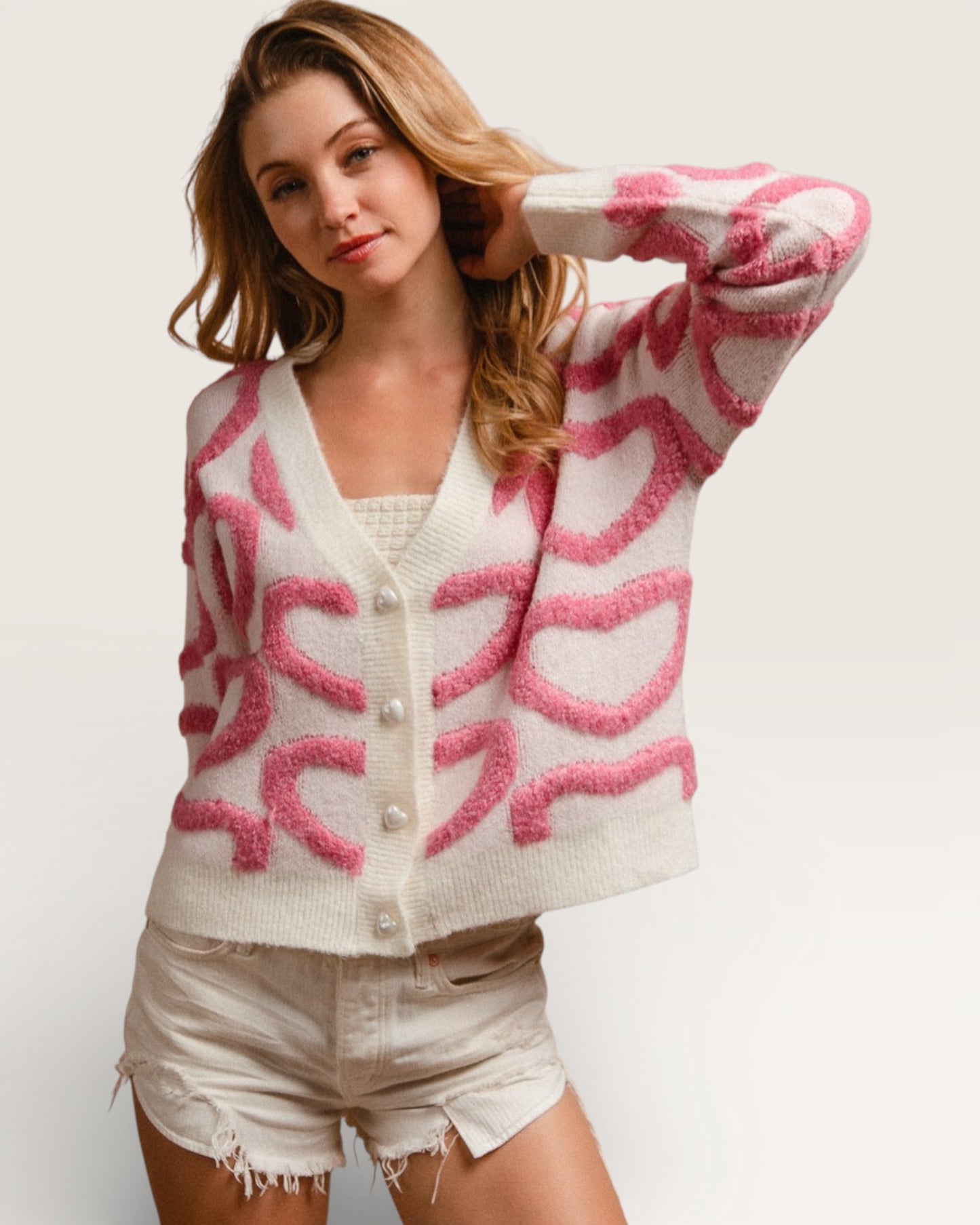 Woman wearing a white cardigan with pink pattern on a plain background