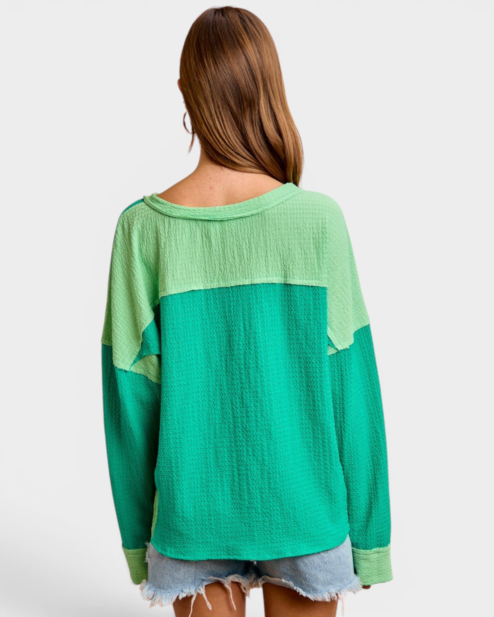 Green and teal color-blocked long-sleeve top worn by a person on a white background