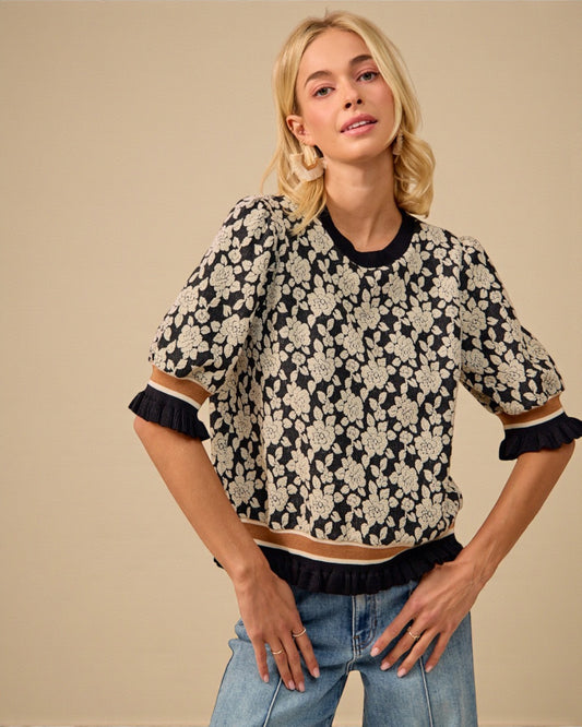 Woman wearing a black and white floral patterned top with blue jeans on a beige background