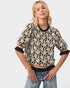 Woman wearing a black and beige floral patterned top with rolled-up sleeves on a light gray background