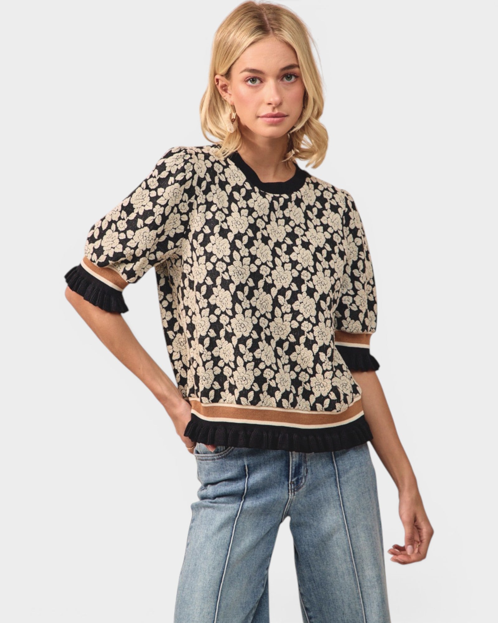 Woman wearing a floral patterned sweater and jeans on a plain background