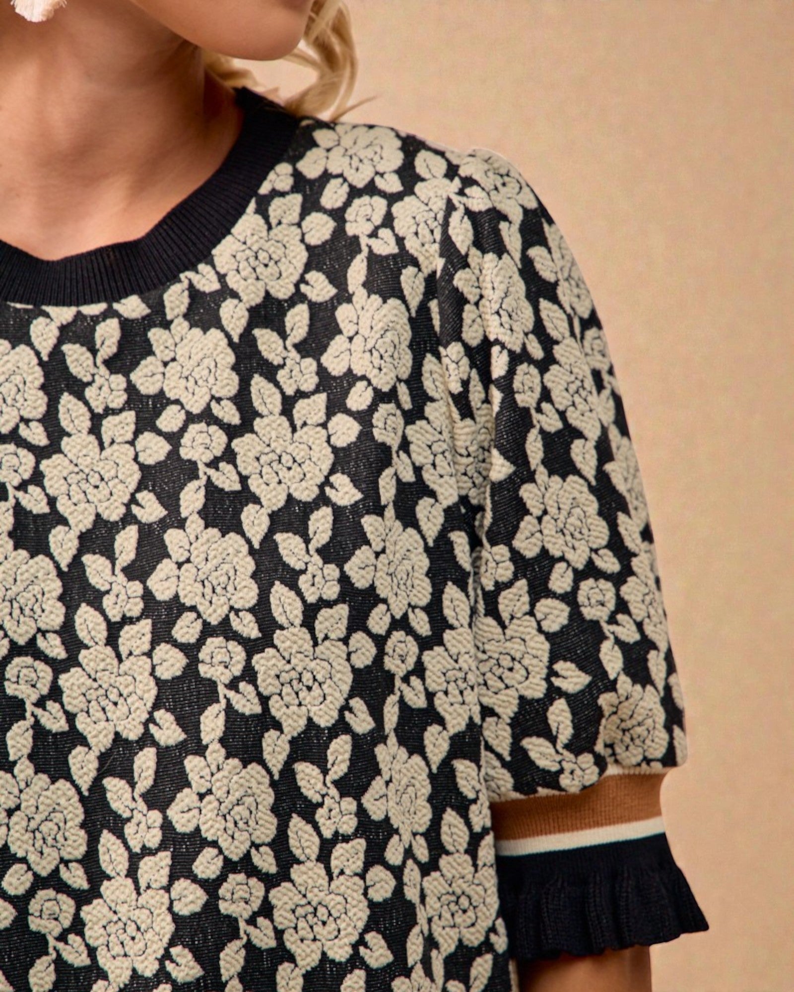 Black sweater with white floral pattern on a beige background