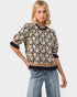 Woman wearing a floral patterned sweater and jeans on a plain background