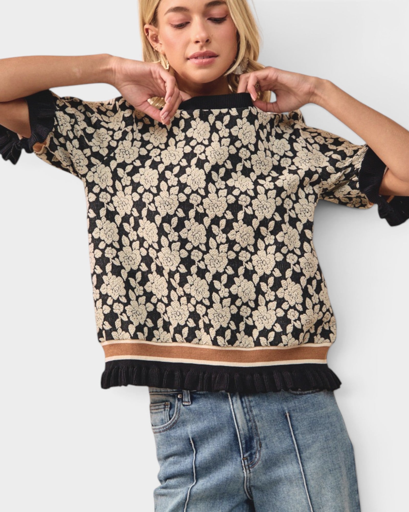 Woman wearing a black and beige floral patterned top with rolled-up sleeves on a white background