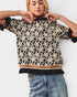 Woman wearing a black and beige floral patterned top with rolled-up sleeves on a white background