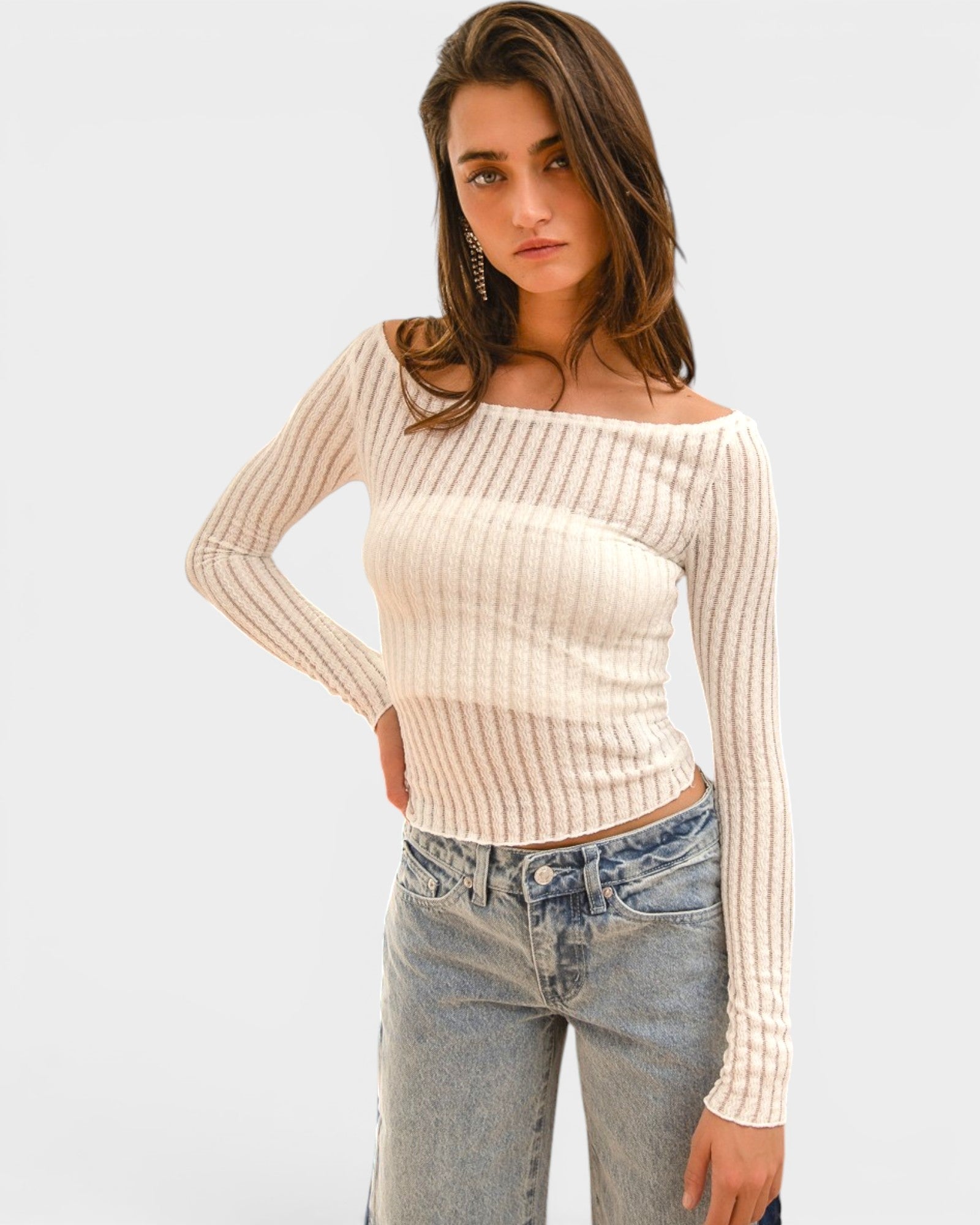 Woman wearing a beige ribbed sweater and blue jeans against a light gray background