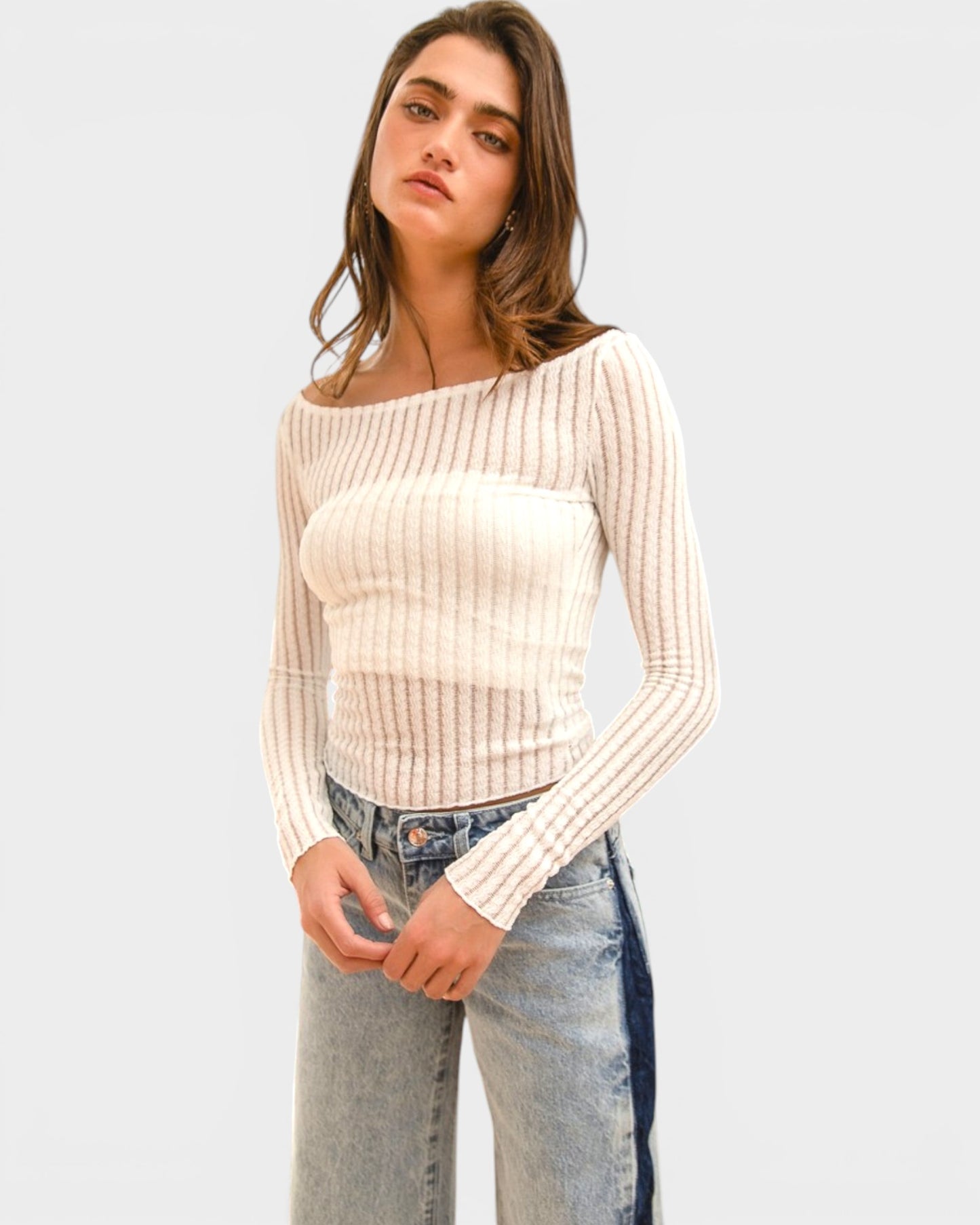 Woman wearing a beige ribbed sweater and jeans on a light gray background