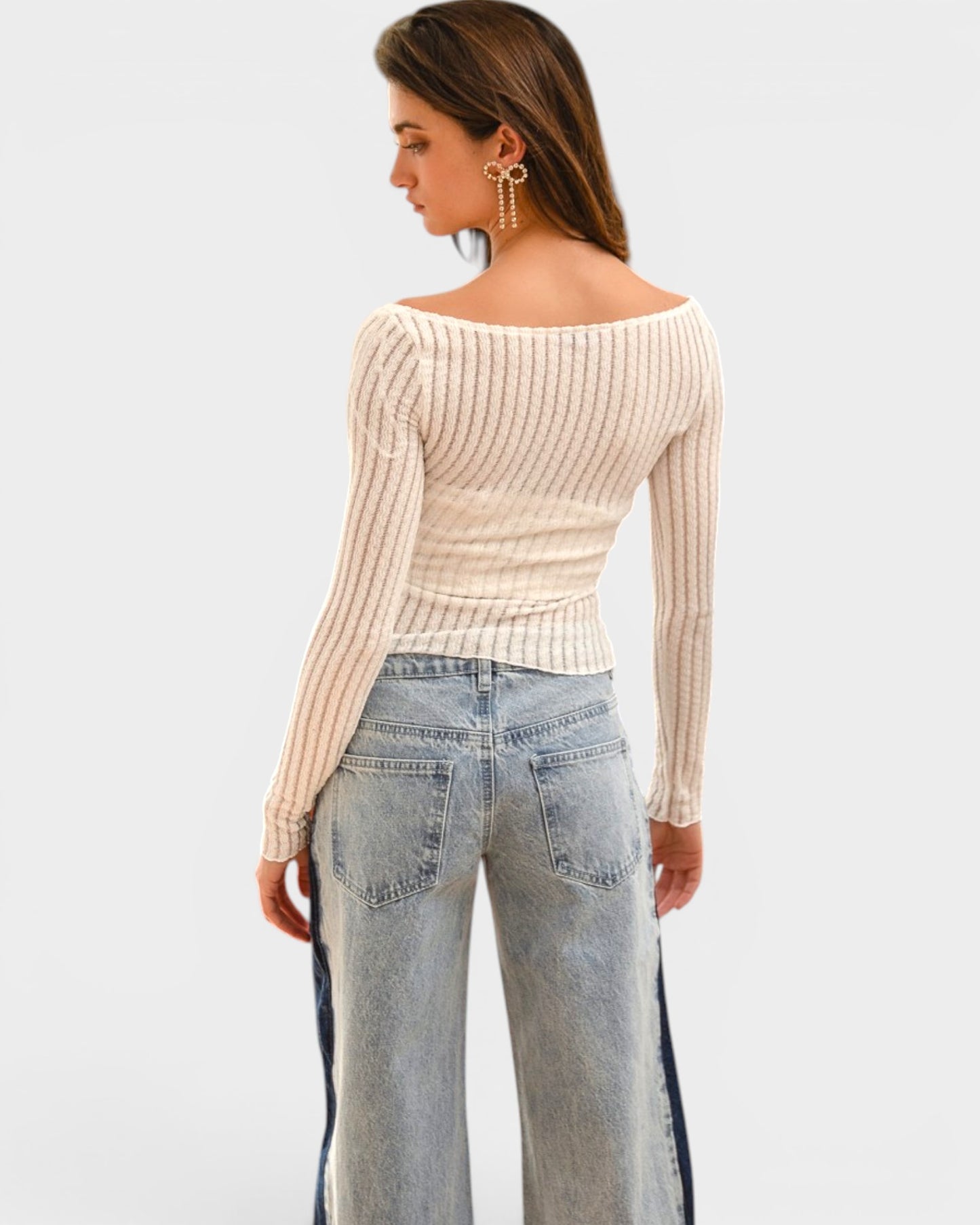 Woman wearing a beige ribbed sweater and light blue jeans on a white background