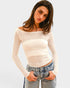Woman wearing a white ribbed sweater and denim shorts on a light gray background