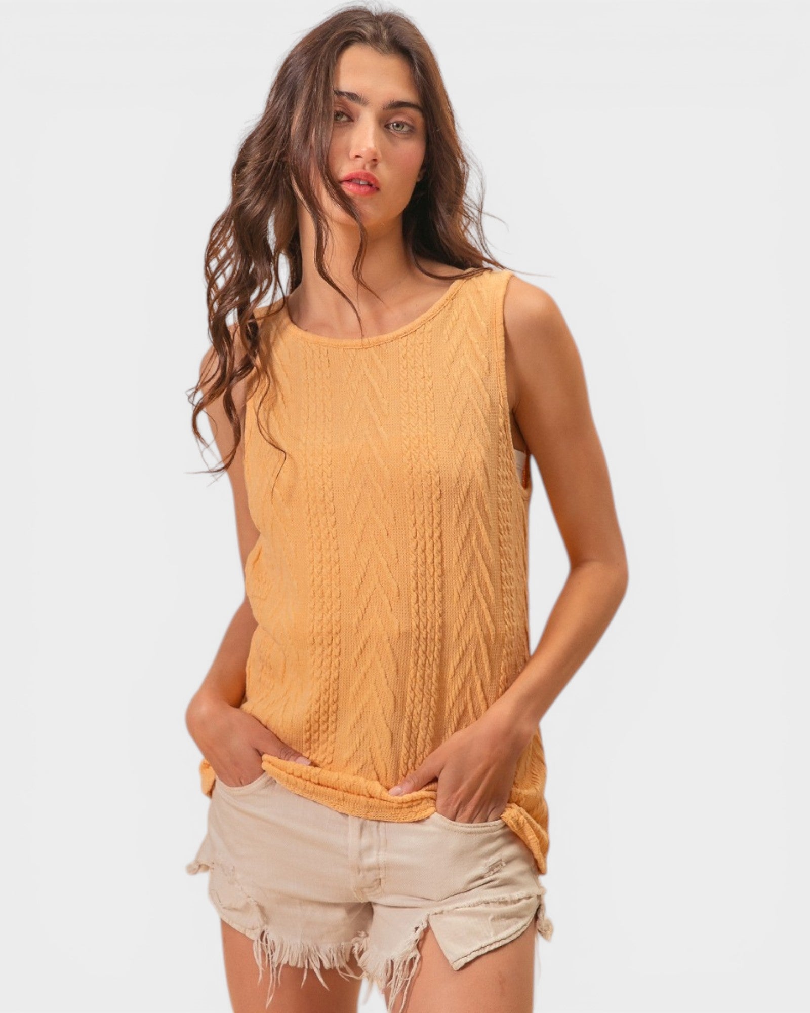 Woman wearing a mustard yellow sleeveless top and beige shorts on a white background