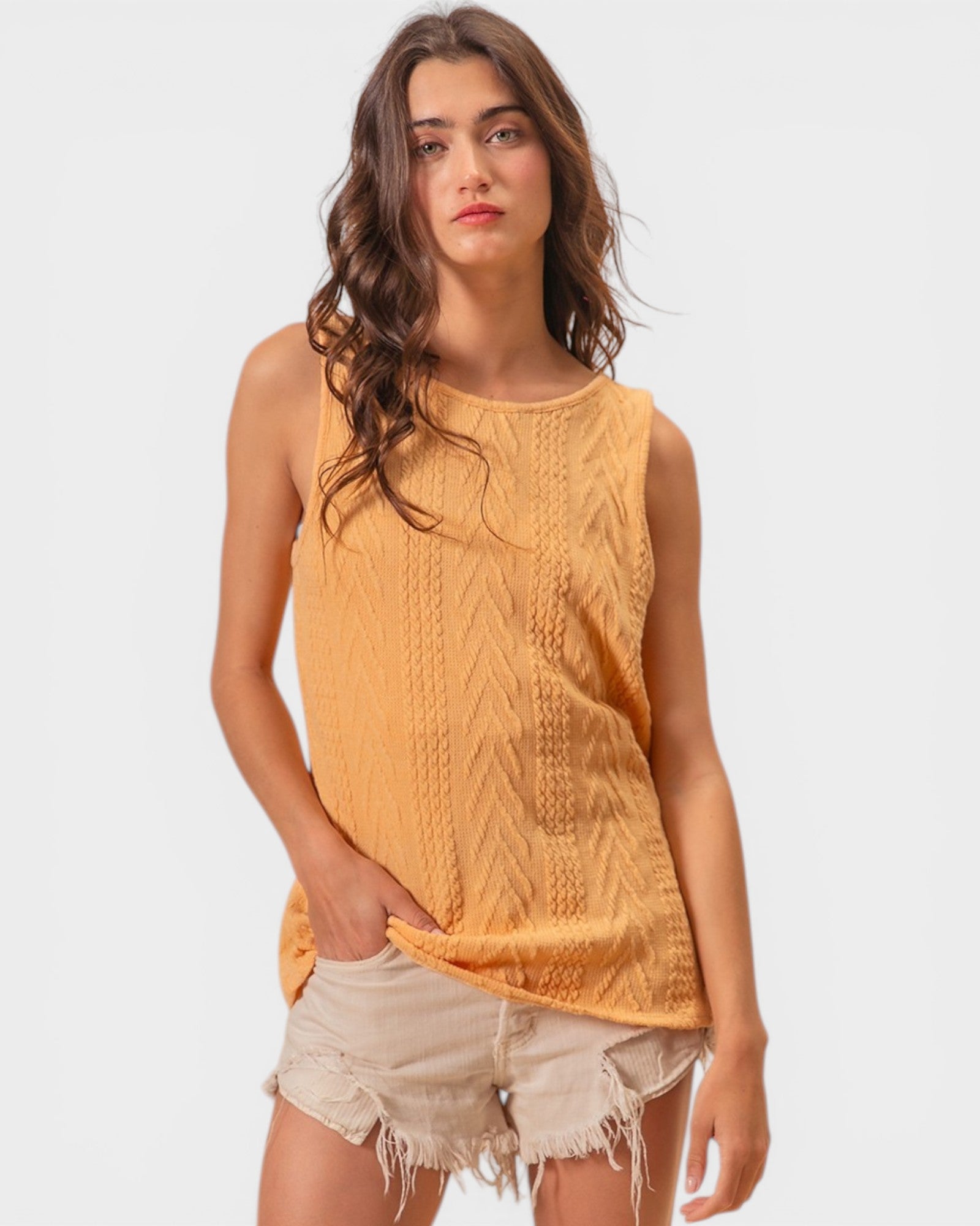Woman wearing a mustard yellow sleeveless top with a white background