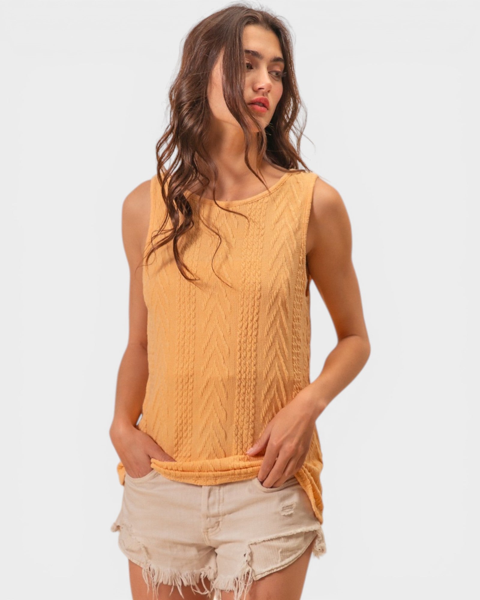 Woman wearing a mustard yellow sleeveless top with a white background