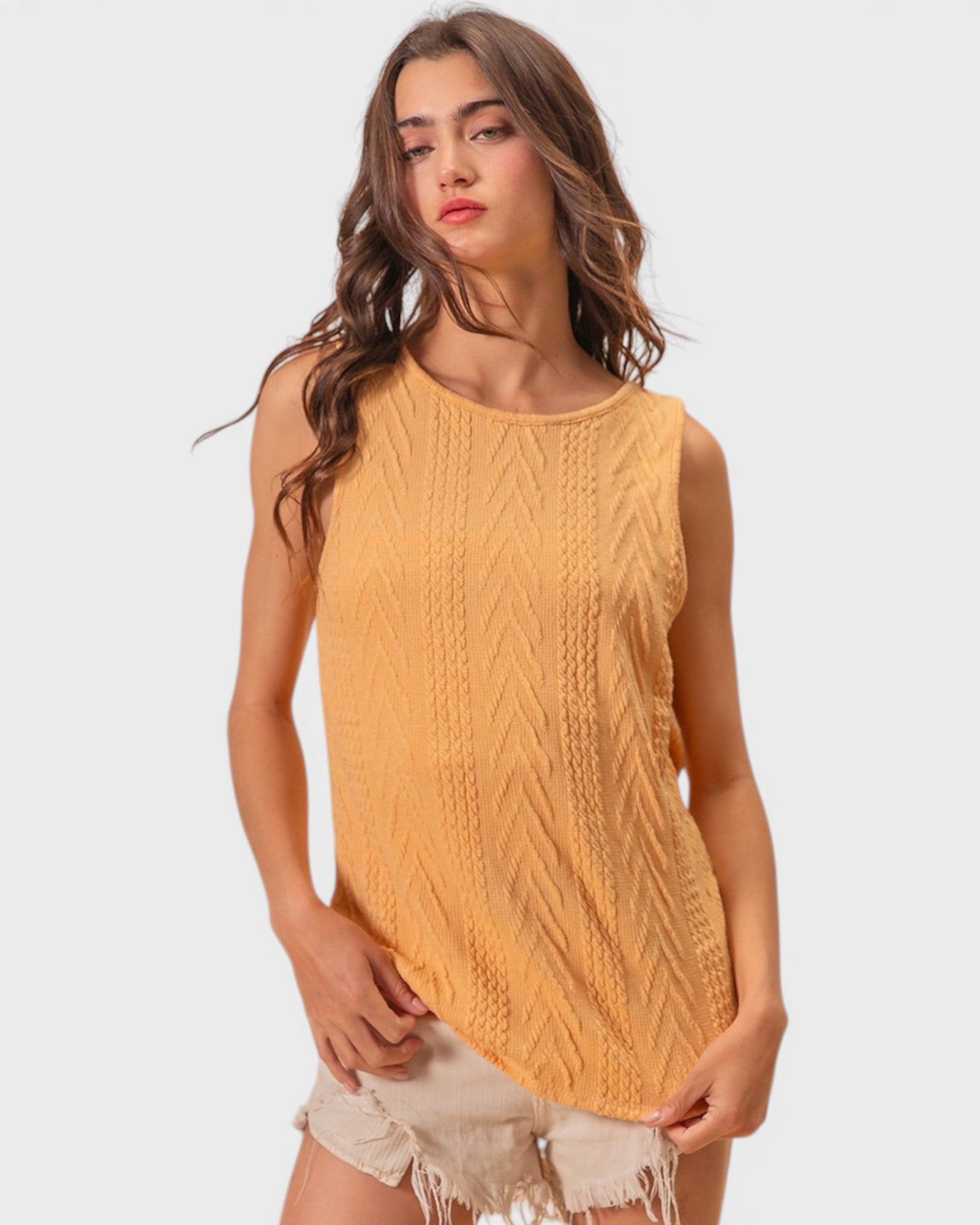 Woman wearing a mustard yellow sleeveless knitted top on a white background