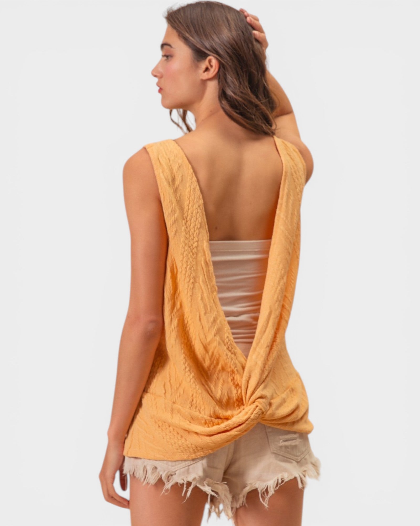 Woman wearing a yellow open-back top and beige shorts on a white background