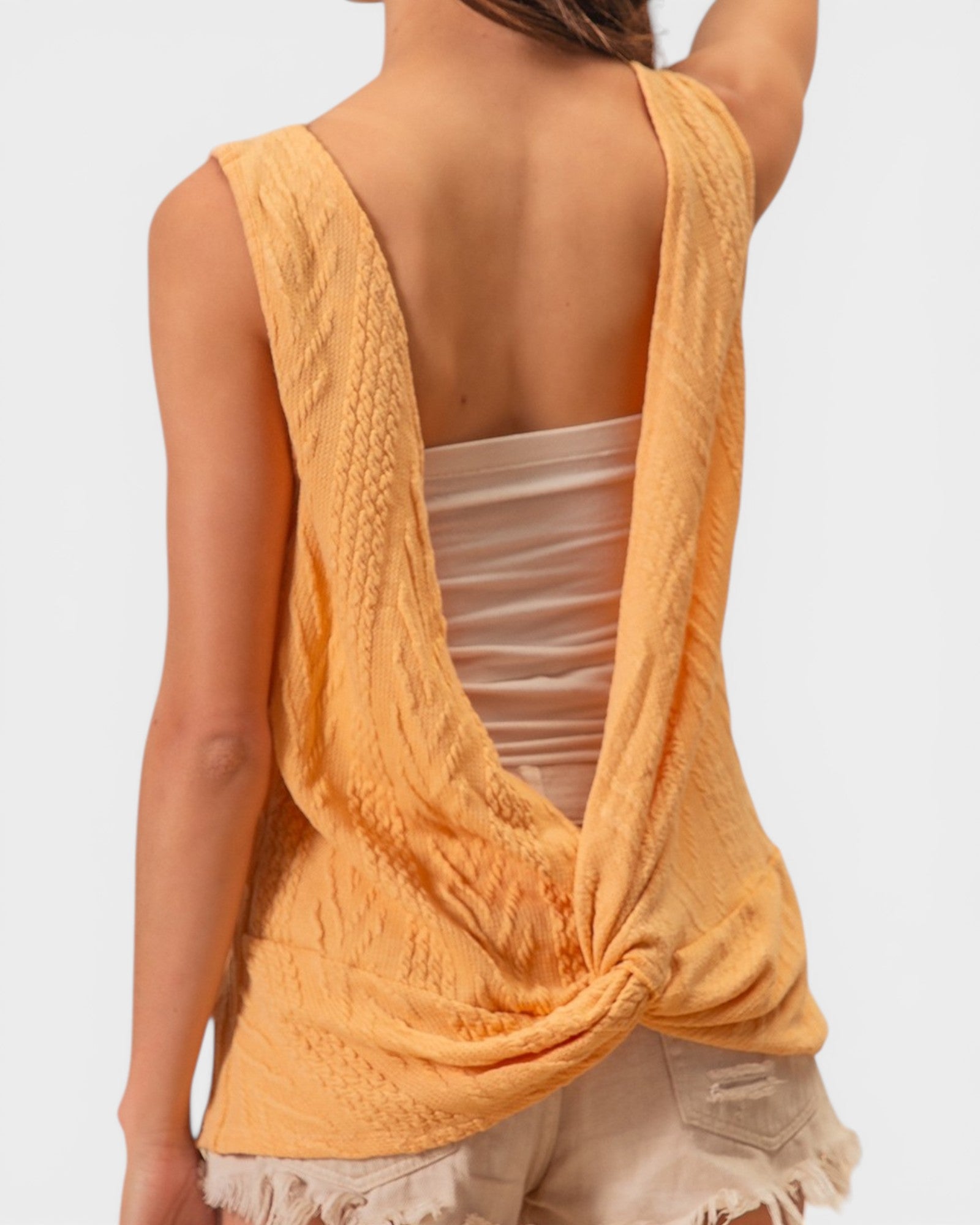 Yellow sleeveless top over a white tank top on a plain background