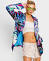 Woman wearing a colorful jacket, white top, and beige shorts against a white background
