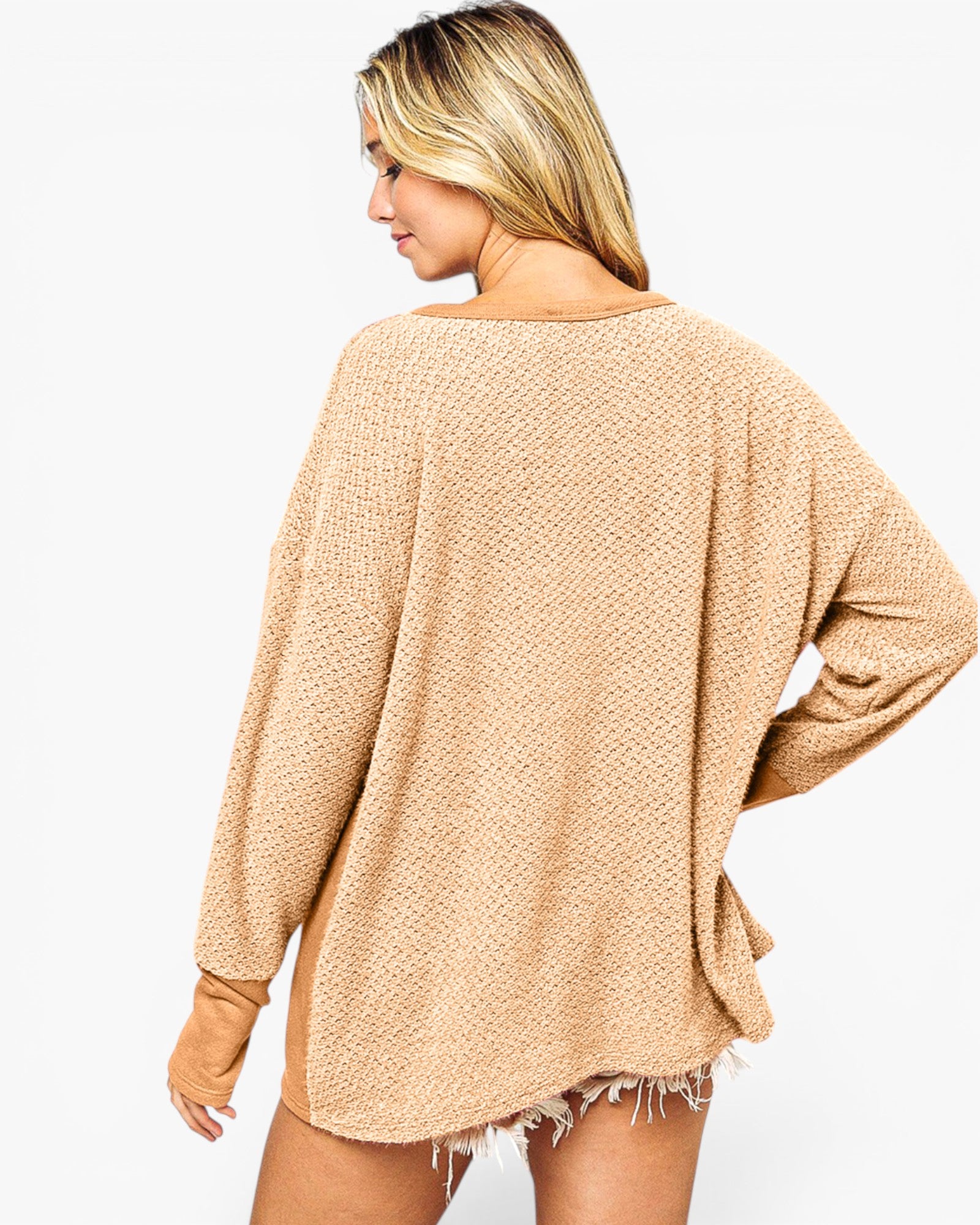 A woman shown from the back wearing a loose, oversized knit sweater in a warm beige or tan color, photographed against a plain light gray studio background.