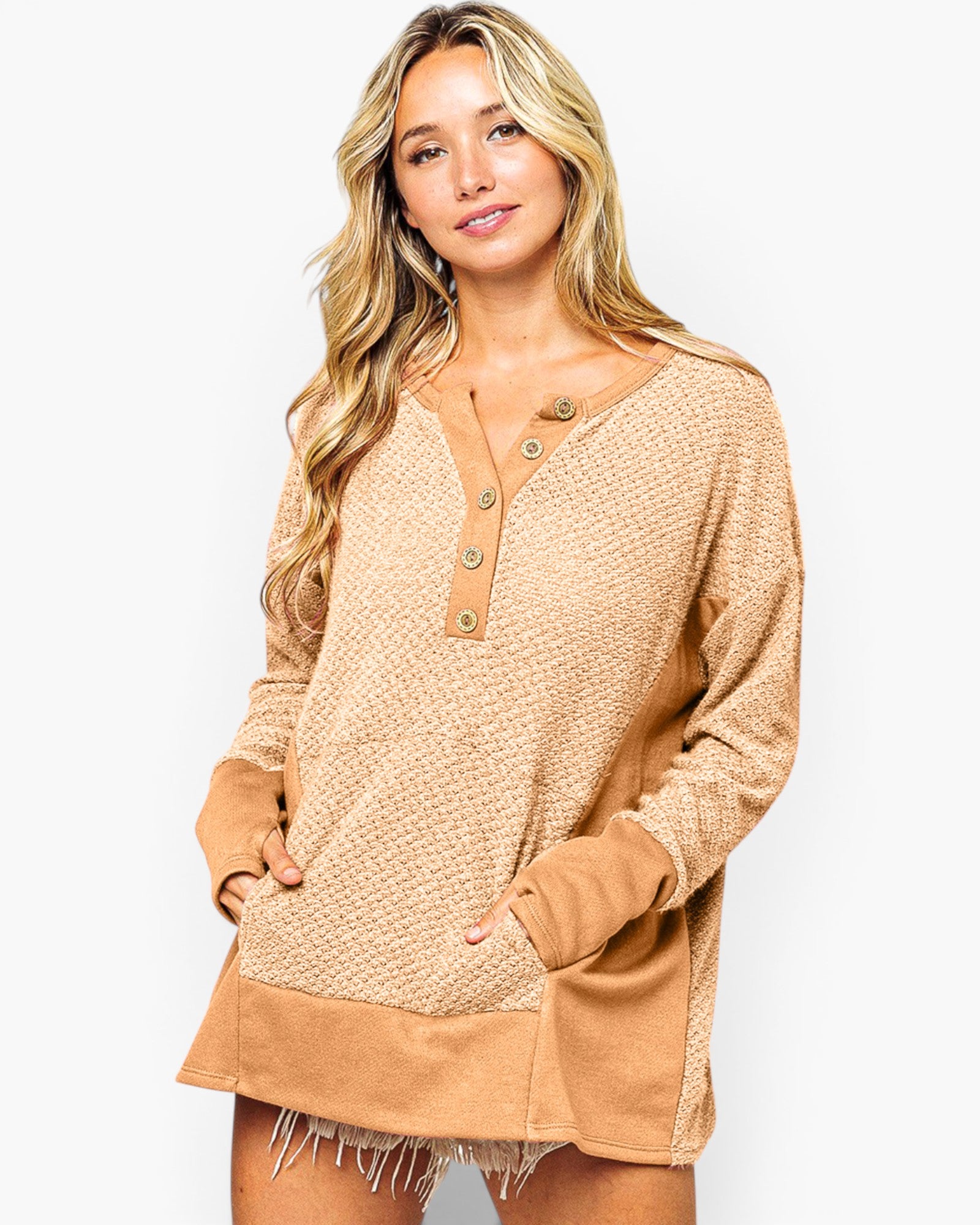 A woman modeling a tan and beige textured knit long-sleeve henley top with button details down the front, set against a plain light gray background.