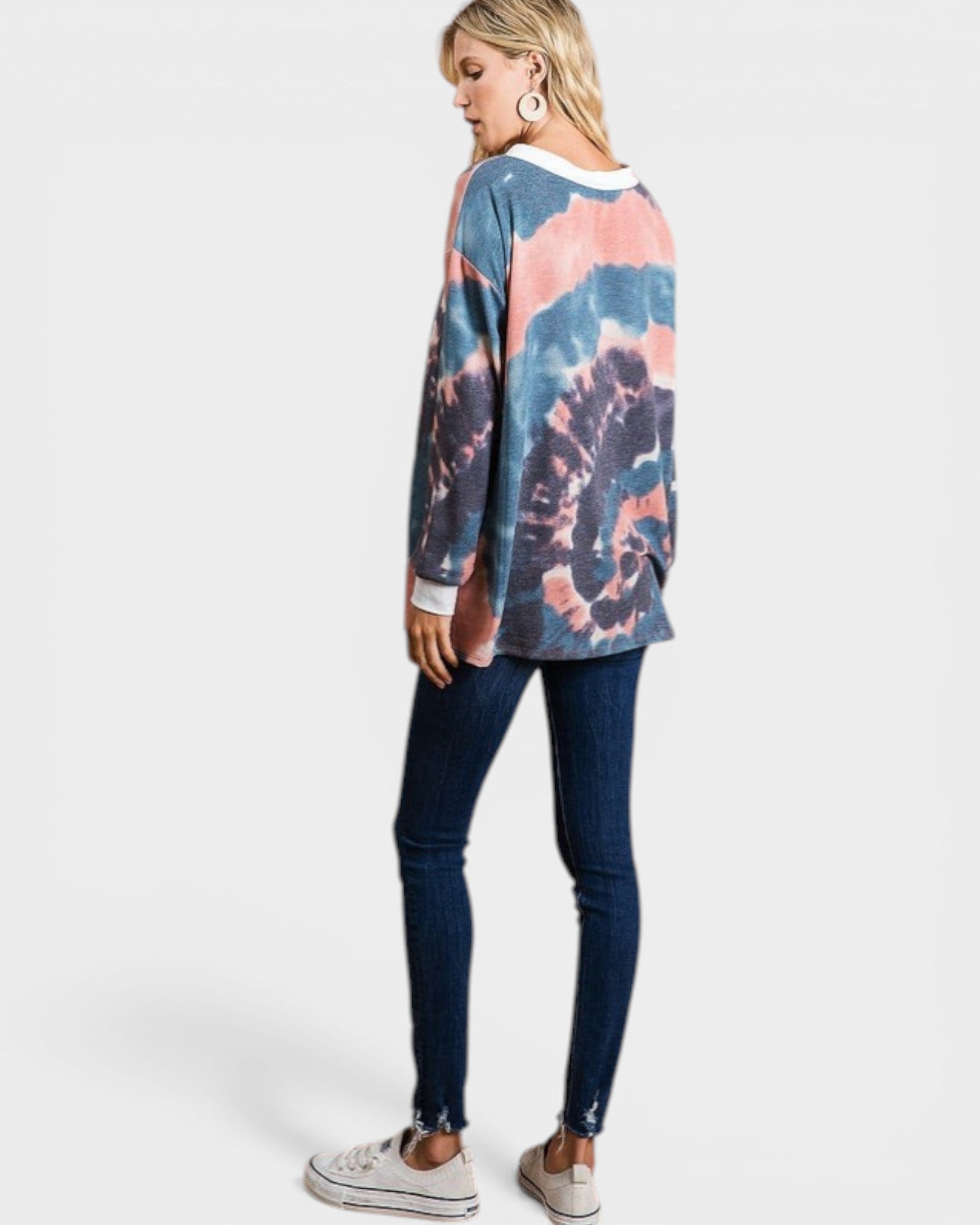 Woman wearing a tie-dye sweater and dark jeans on a white background