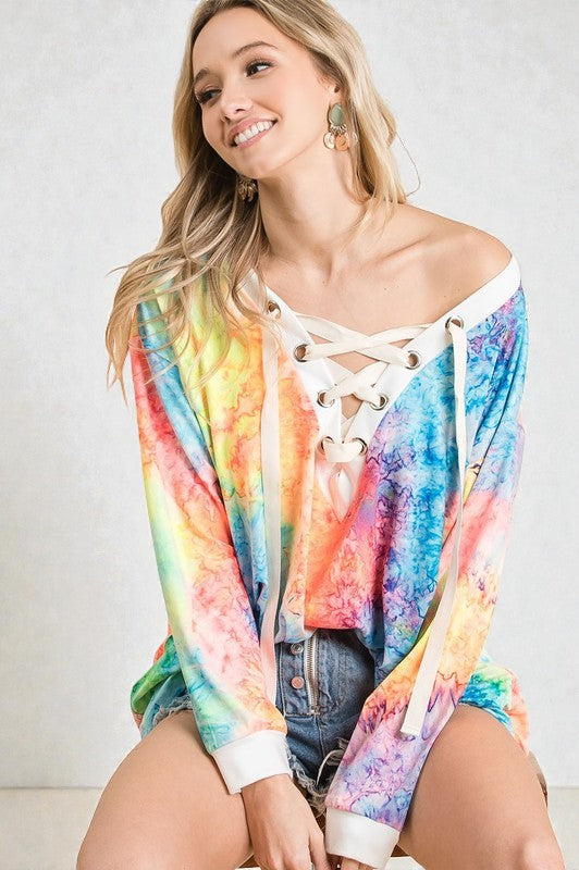 Woman wearing a colorful tie-dye off-shoulder top with lace-up details on a plain background
