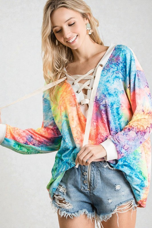 Woman wearing a colorful tie-dye hoodie and denim shorts on a plain background