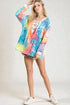 Woman wearing a colorful tie-dye hoodie with a white lace top underneath on a plain background